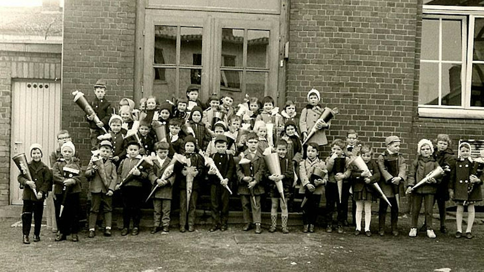 Ein Schwarzweißfoto zeigt Kinder mit Schultüten vor einem Schulgebäude. Das Foto ist vor 60 Jahren entstanden.