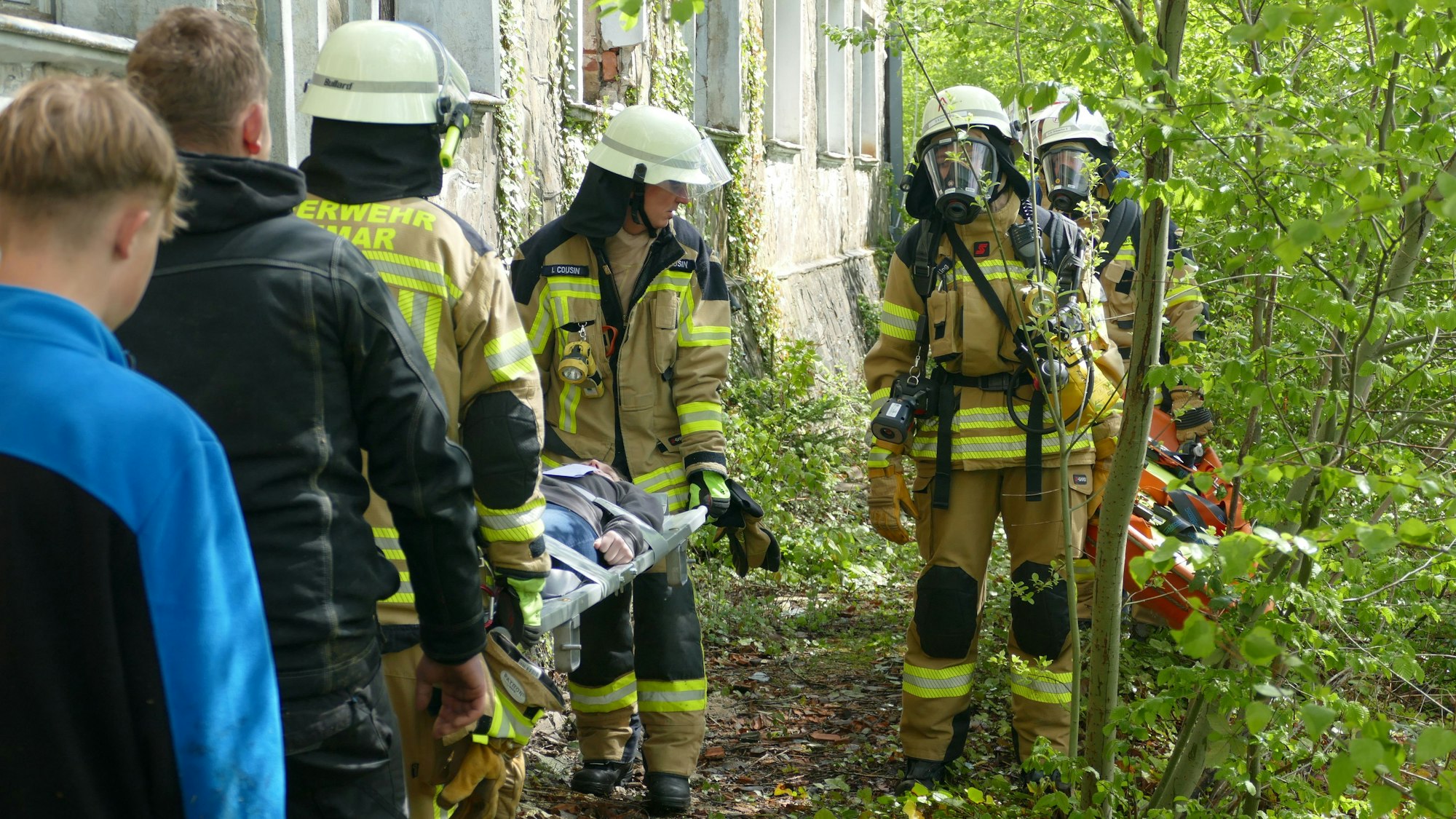 Feuerwehrleute tragen eine verletzte Person durch ein Gebüsch.