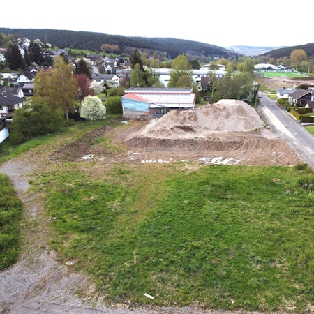 Blick auf das Grundstück mit der kaputten Turnhalle und einem großen Schutthaufen.