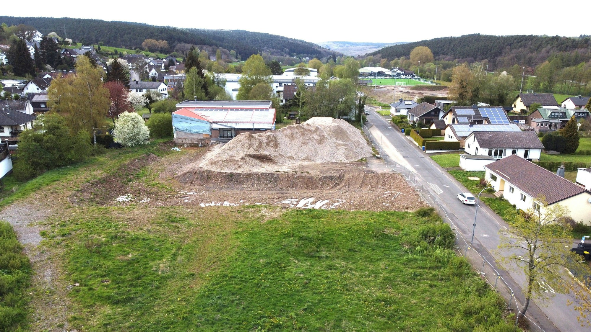 Blick auf das Grundstück mit der kaputten Turnhalle und einem großen Schutthaufen.