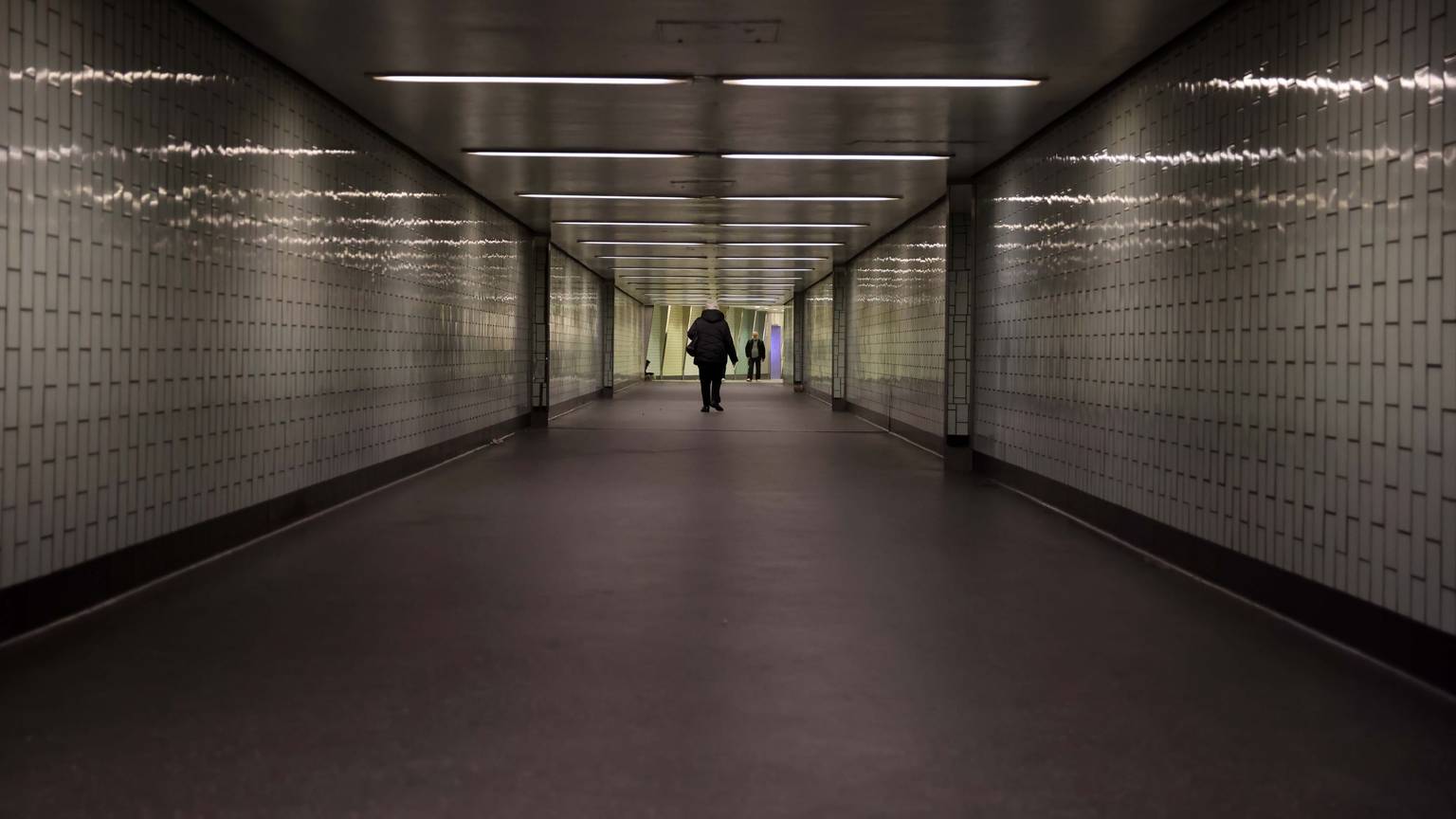 Eine Person geht durch einen langen Tunnel, der nicht hell beleuchtet ist.