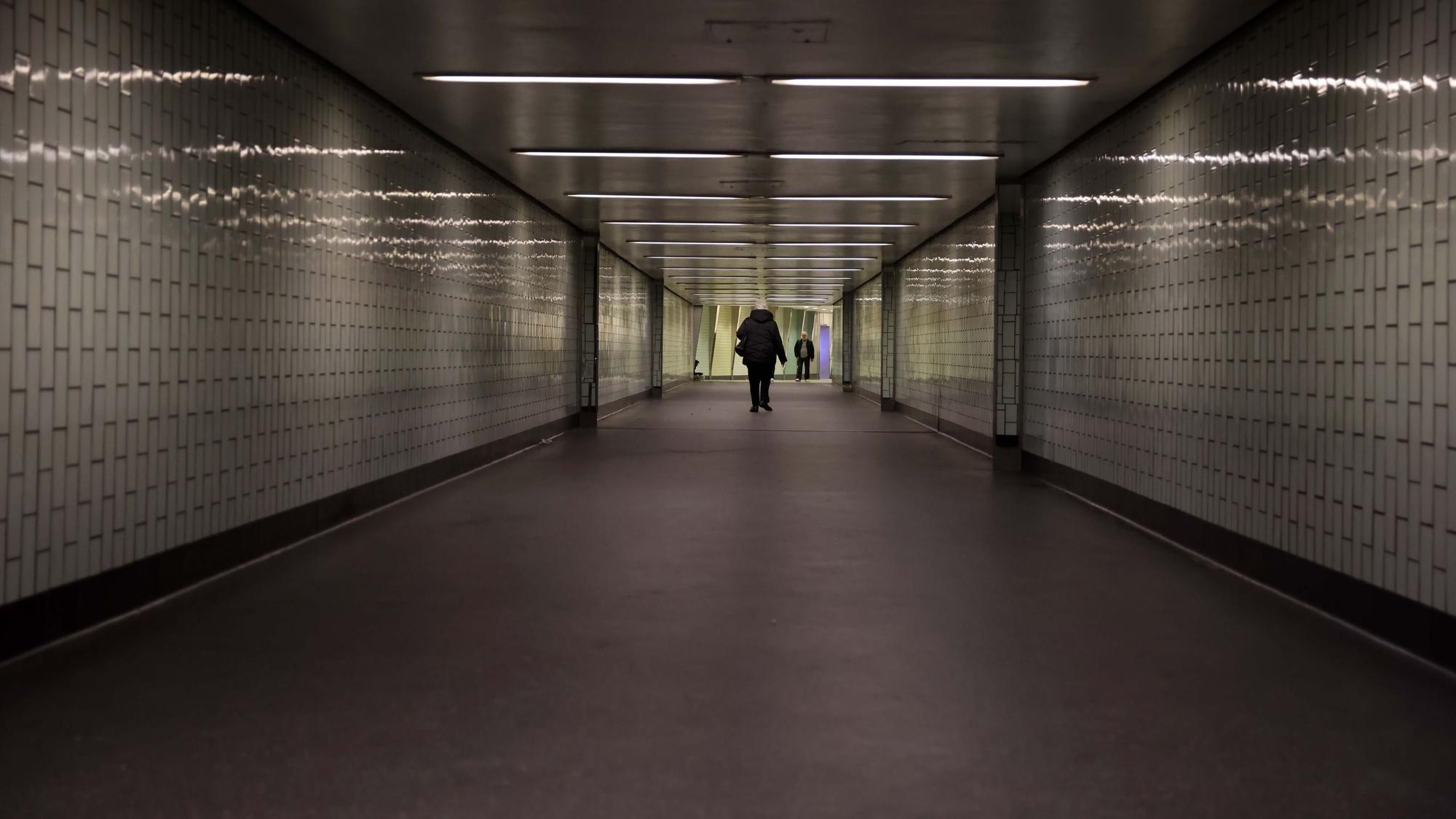 Eine Person geht durch einen langen Tunnel, der nicht hell beleuchtet ist.