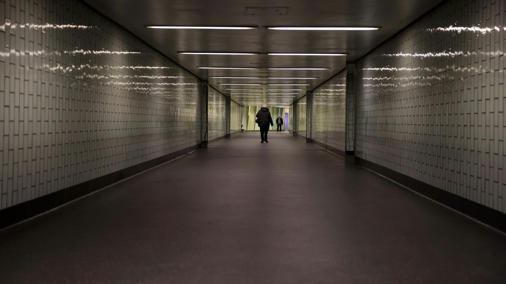 Eine Person geht durch einen langen Tunnel, der nicht hell beleuchtet ist.