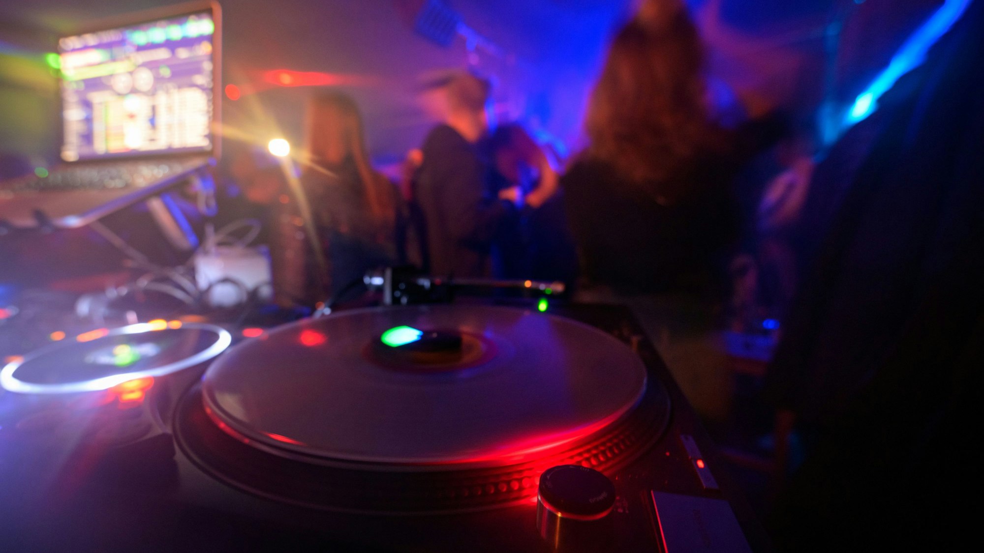 Partygänger tanzen vor einem DJ-Pult.