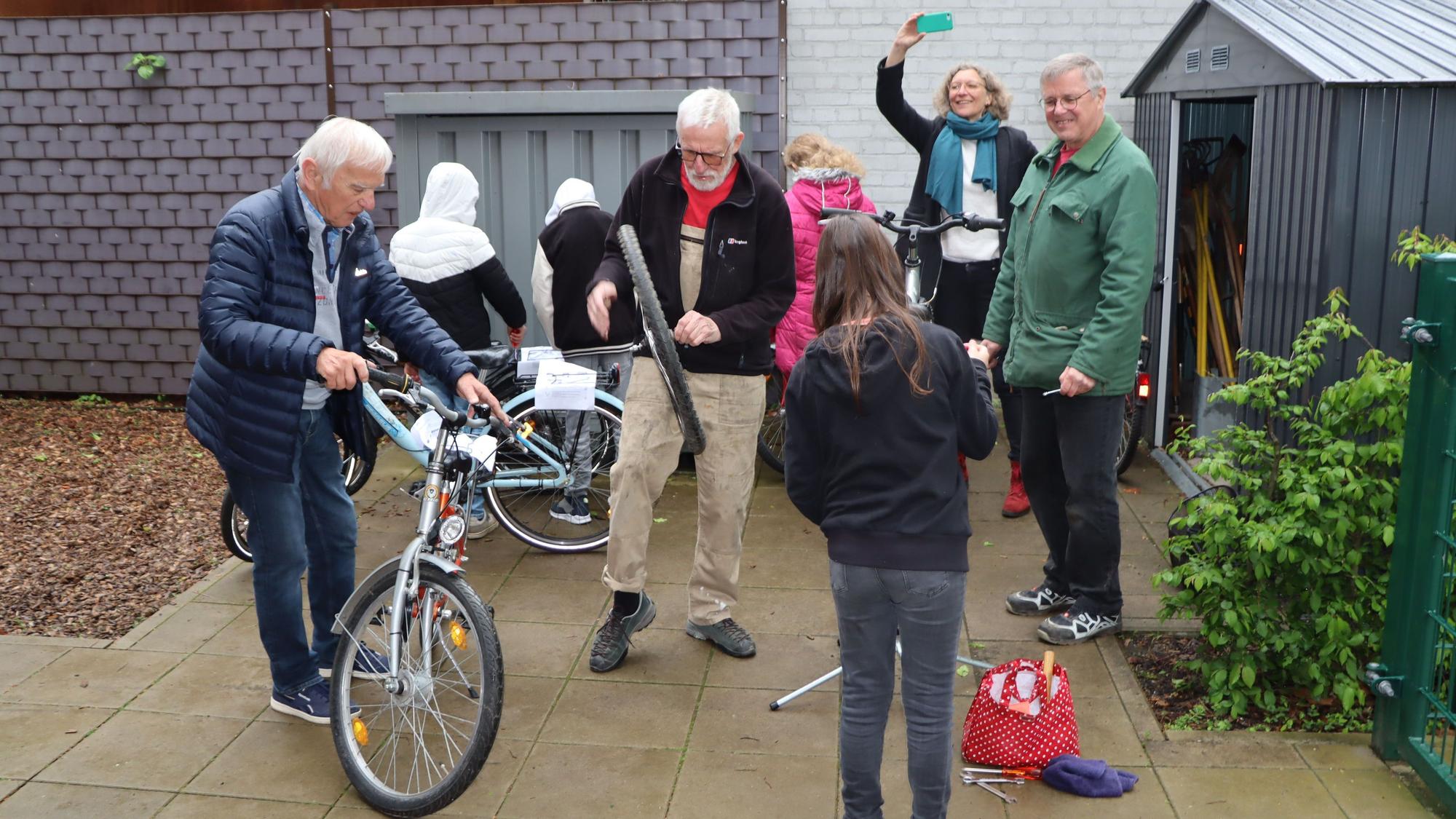 Ehrenamtler vom Repair-Café reparieren zwei Fahrräder. Schülerinnen und Schüler helfen dabei mit.