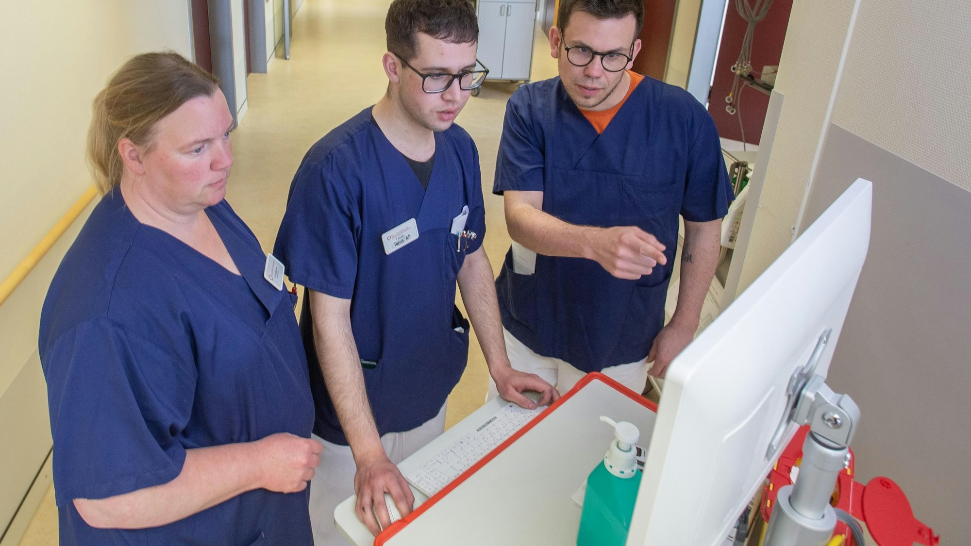 Besprechung: Projektleiter Jonas Sebastian Schütter Gesundheits- und Bildungszentrum des Klinikums Oberberg (rechts) mit Schüler Ilyas Chaibi aus Marienheide und Praxisanleiterin Nicole Wurzbacher. Die Gruppe steht an einem Computer auf dem Klinikflur.