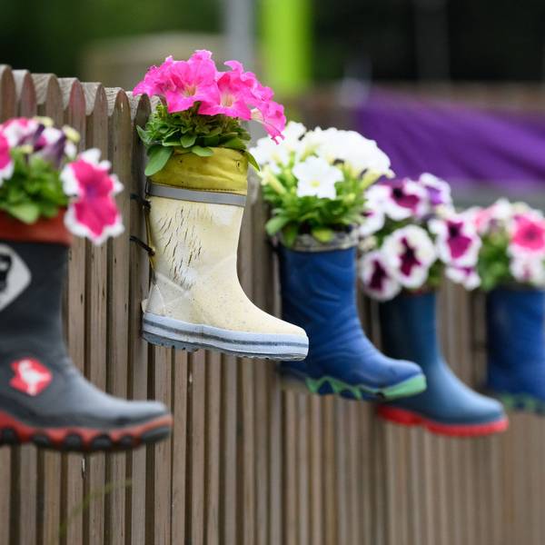 Kinder-Gummistiefel mit Blumen hängen an einem Zaun einer Kindertagesstätte.