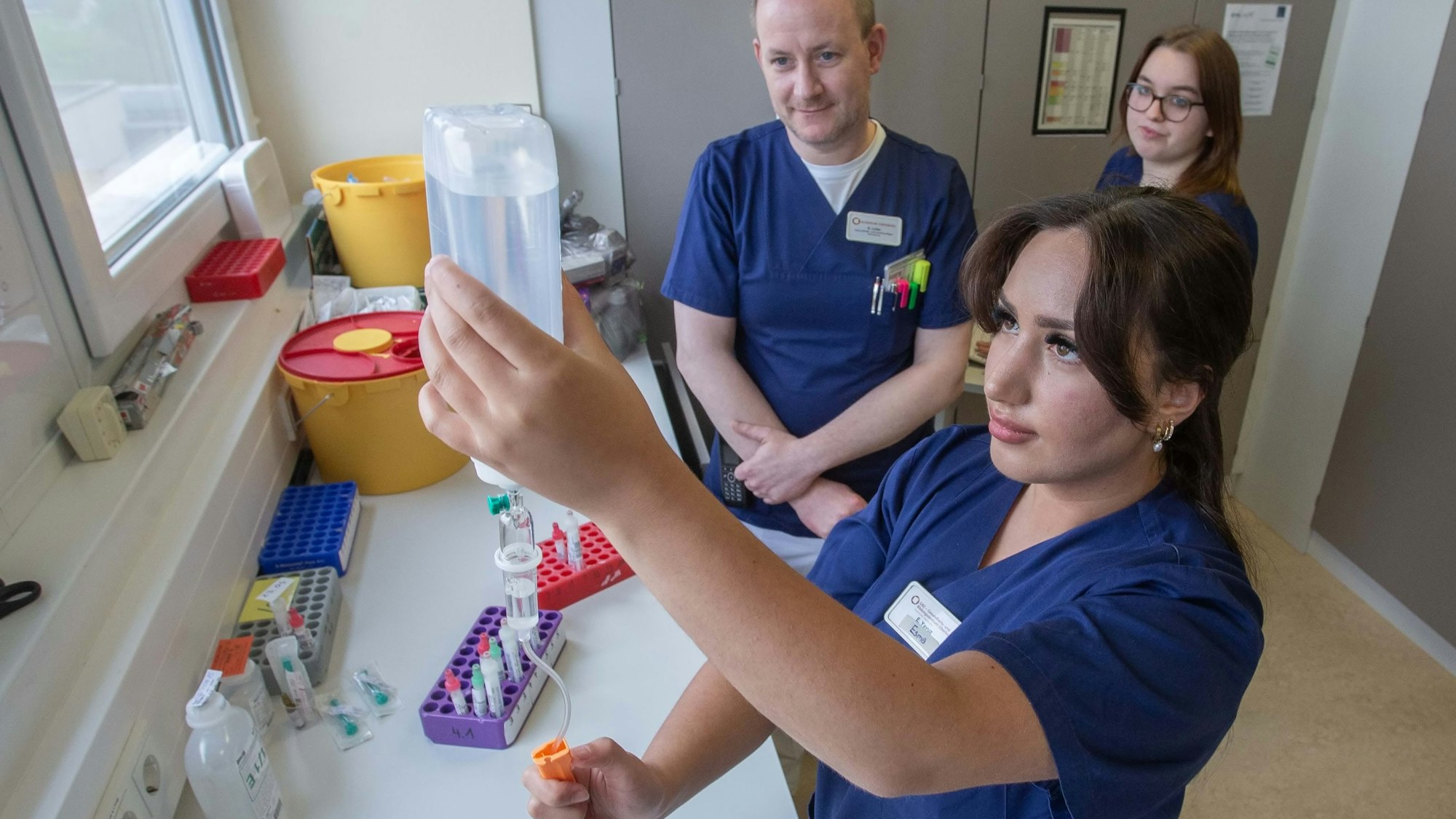 Auch das Vorbereiten von Medikamenten gehört in der Waldbröler Kardiologie zu den Aufgaben der Auszubildenden: Hier macht die Auszubildende Esma Yavuz aus Gummersbach unter Aufsicht von Stationsleiter Daniel Linke eine Infusion fertig. Mitschülerin Zoe Müschenich sieht dabei zu.