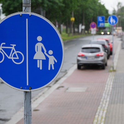 Ein Schild für einen getrennten Rad- und Gehweg steht vor dem Ende eines Radweges und dem Beginn der Zone, in der das Parken auf dem halben Gehweg erlaubt ist.