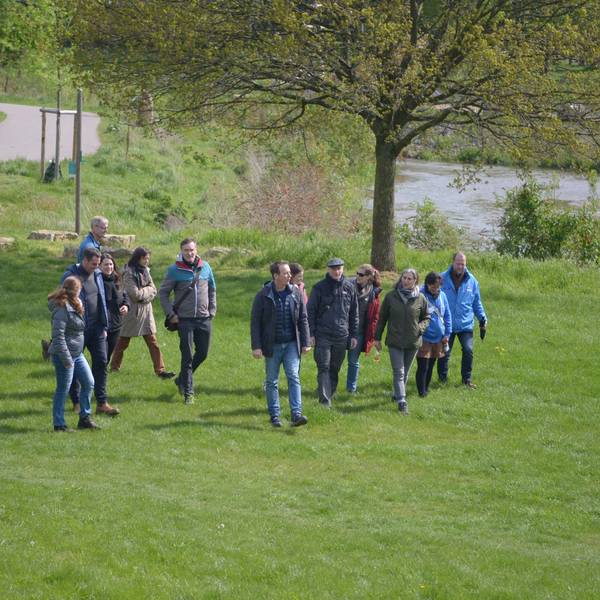 Eine Gruppe von Männern und Frauen geht über eine Wiese, im Hintergrund die Erft.