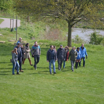 Eine Gruppe von Männern und Frauen geht über eine Wiese, im Hintergrund die Erft.