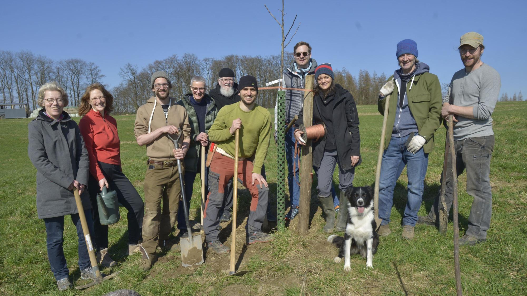 Tatkräftig packen Vorstand Patrick Beyer und die Ehrenamtler beim Pflanzen der Obstbäume auf dem Agro-Forst an. Die Gruppe steht auf einer Wiese beisammen. Alle haben einen Spaten in der Hand.