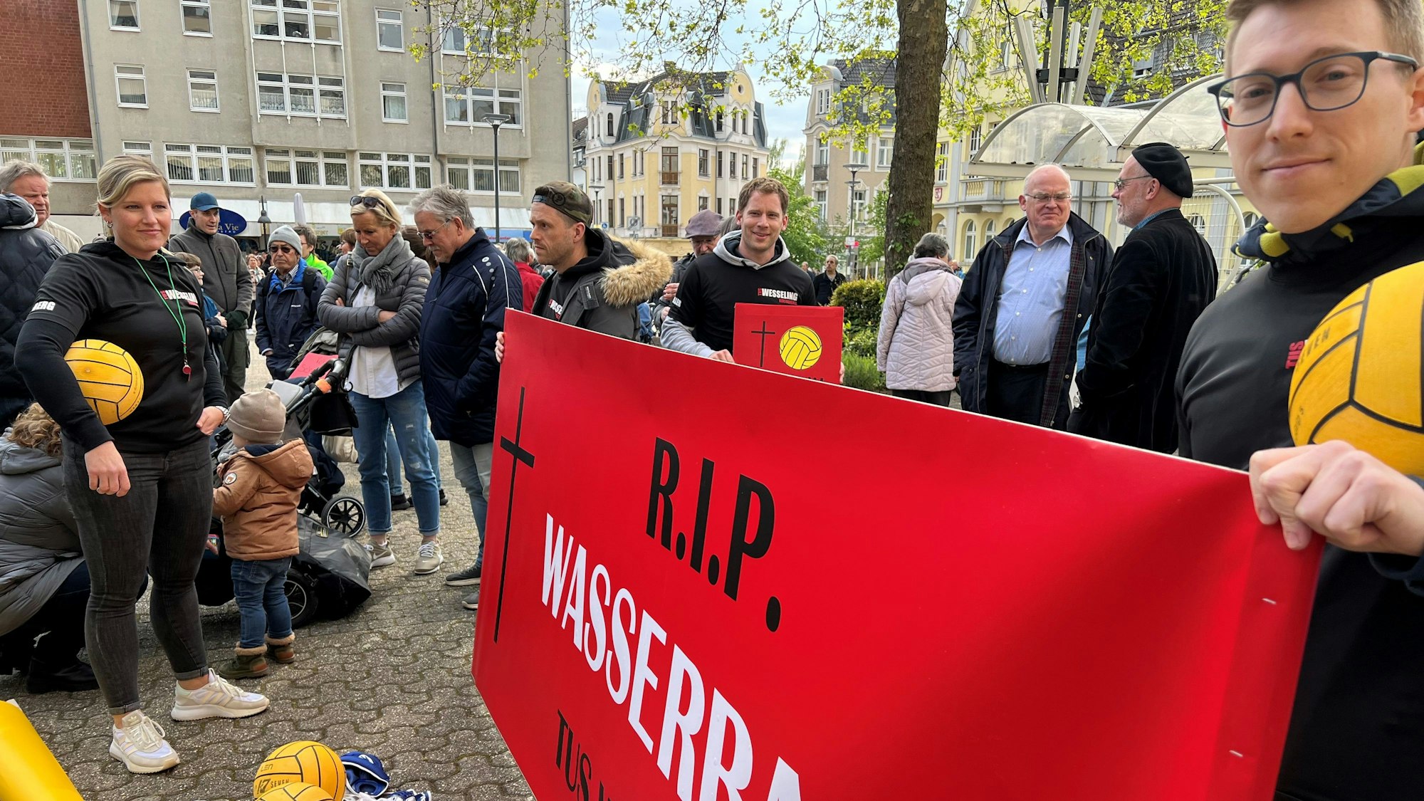 Auf dem Foto sind Wassersportler der TuS Wesseling zu sehen. Sie halten ein rotes Transparent hoch.