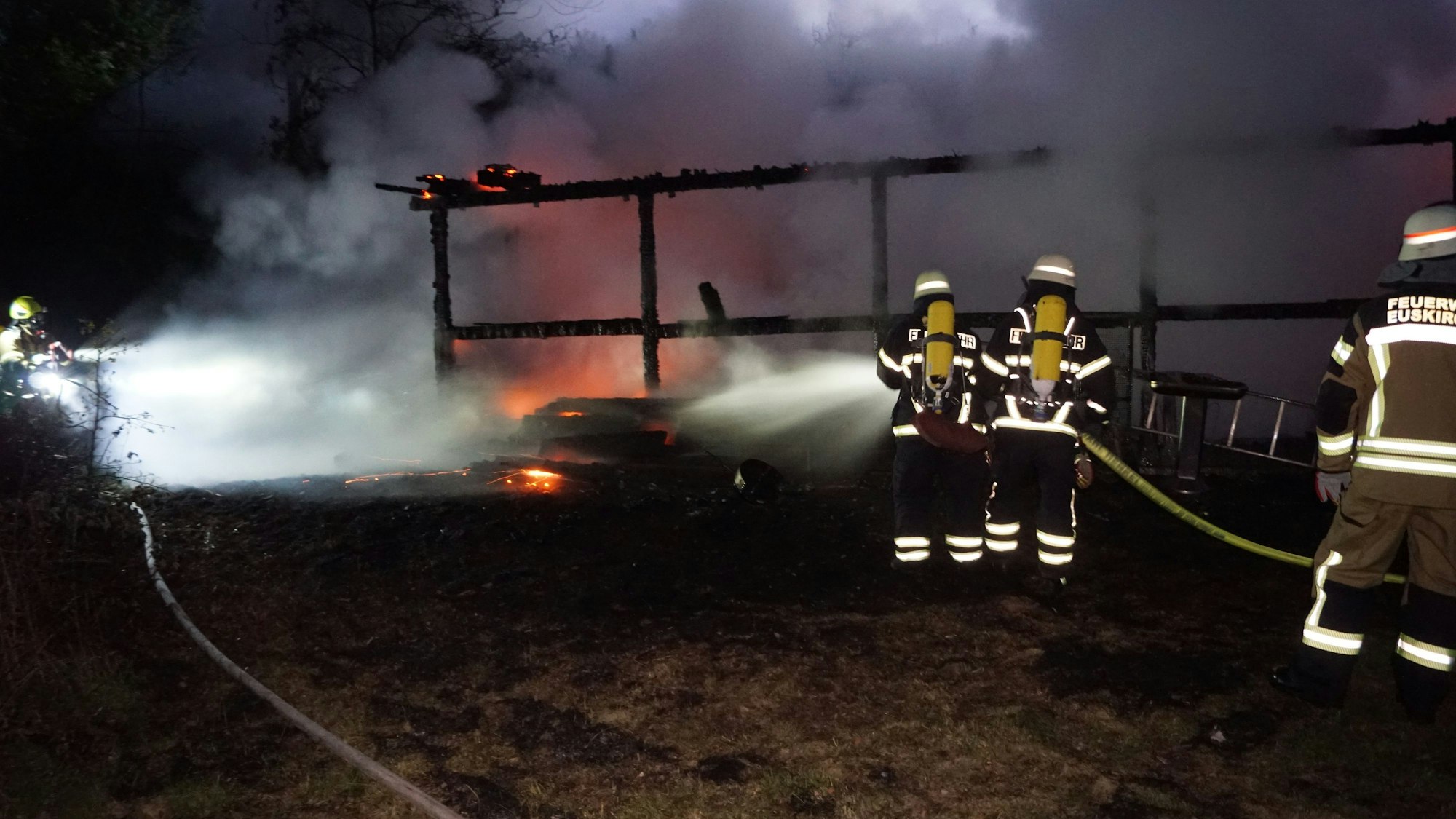Das Bild zeigt, wie Feuerwehrleute die Flammen mit Wasser bekämpfen.