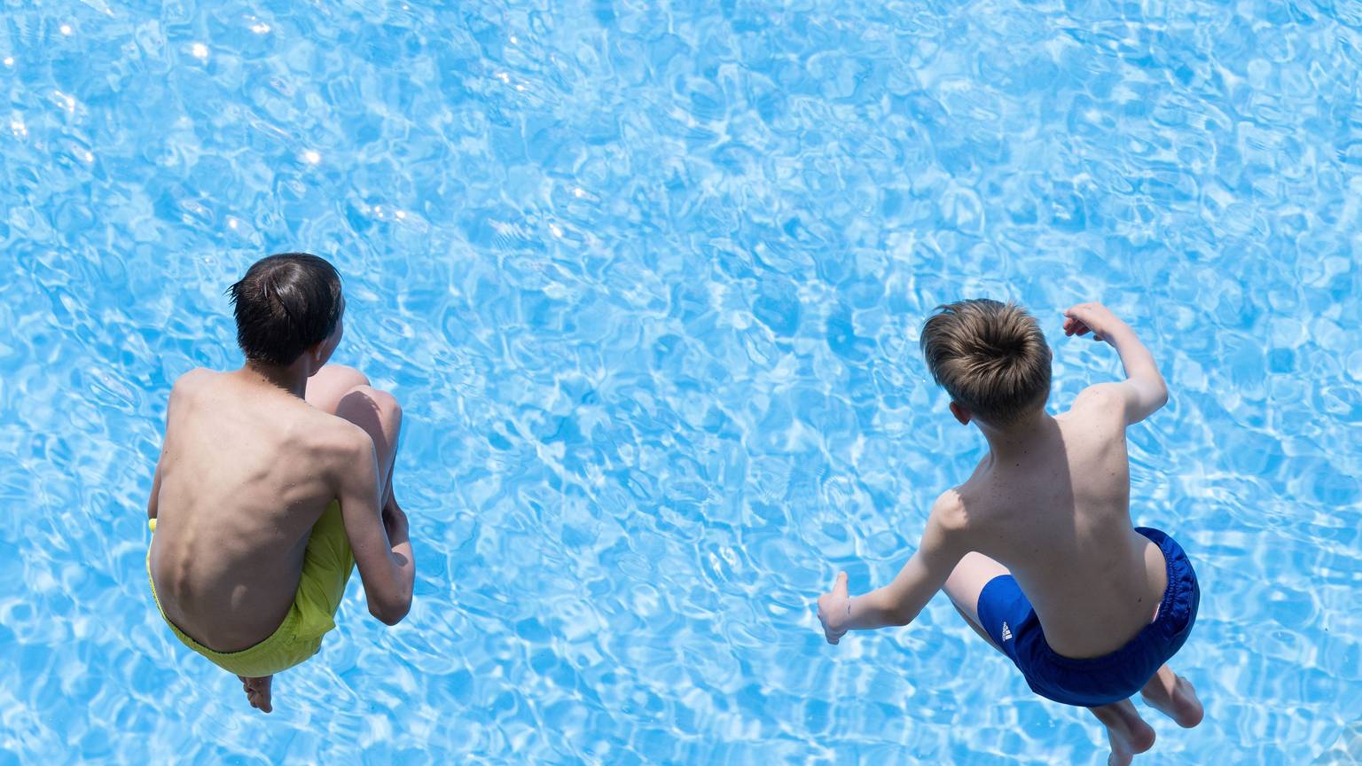 Zwei Jungen springen im Freibad ins Wasser.