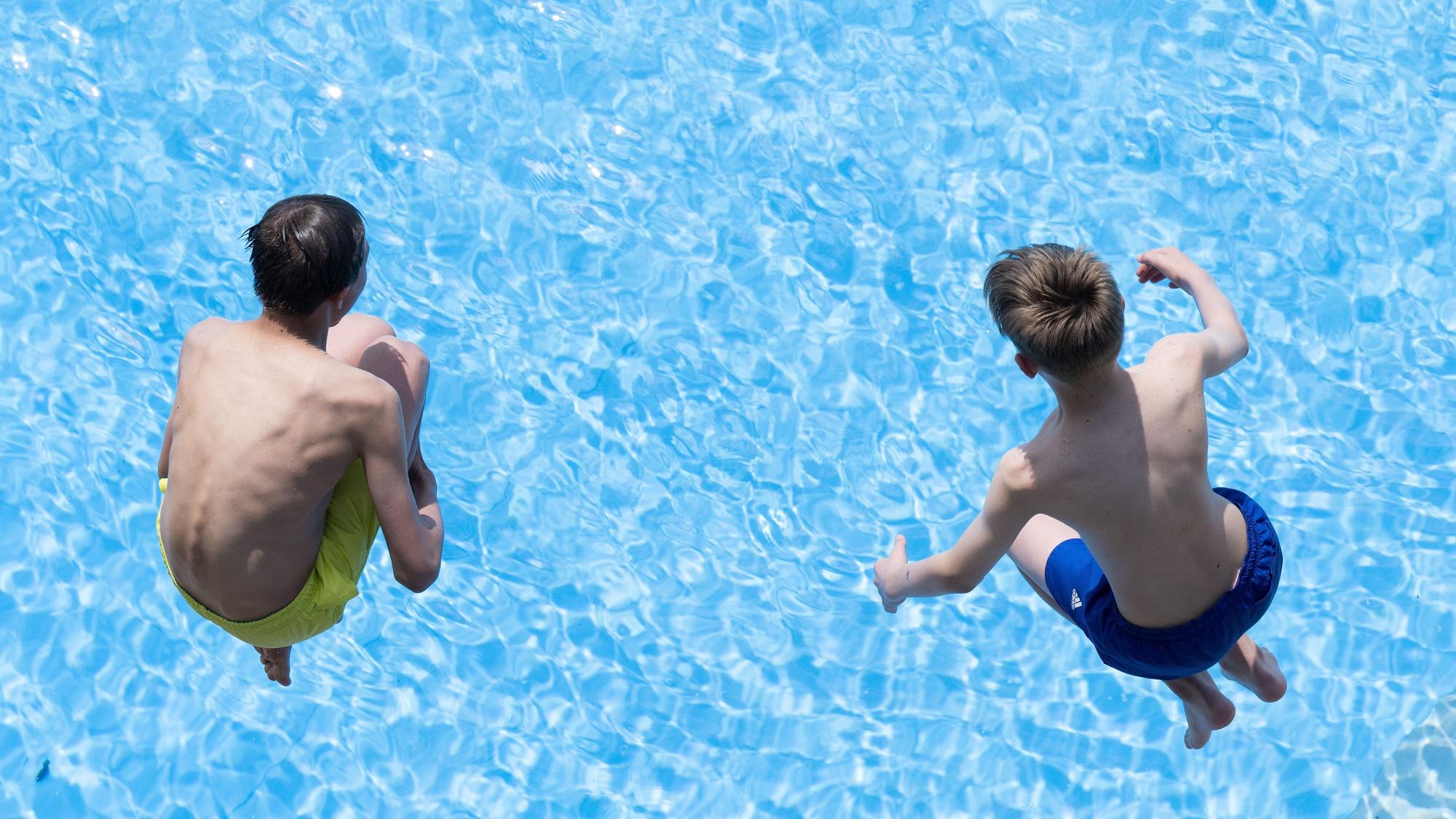 Zwei Jungen springen im Freibad ins Wasser.