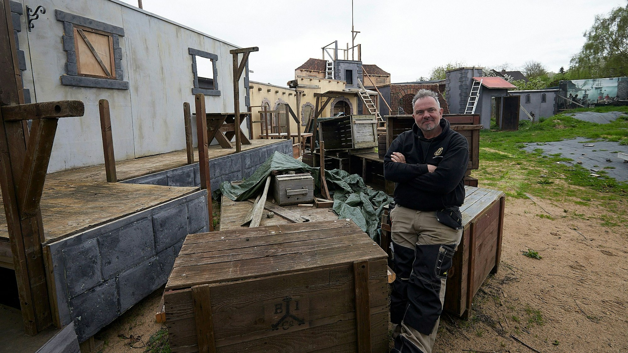 Ralf Winterhoff sitzt auf einer großen Holzkiste. Im Hintergrund sind mehrere Bühnen mit typischen Piratenkulissen zu sehen.