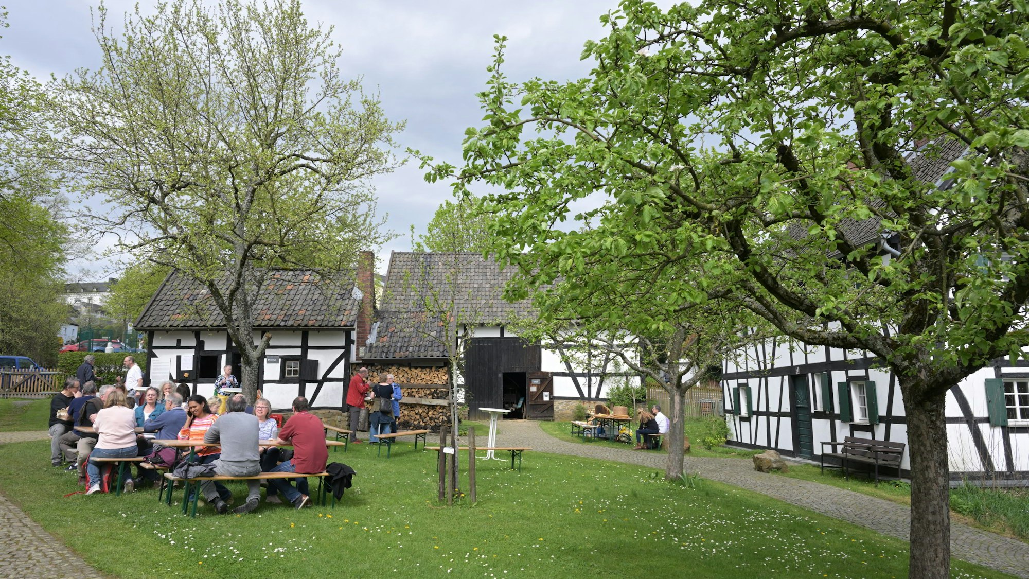 Auf Bänken an Biertischen sitzen Besucher vor der Kulisse der Fachwerkhäuser des Museums.
