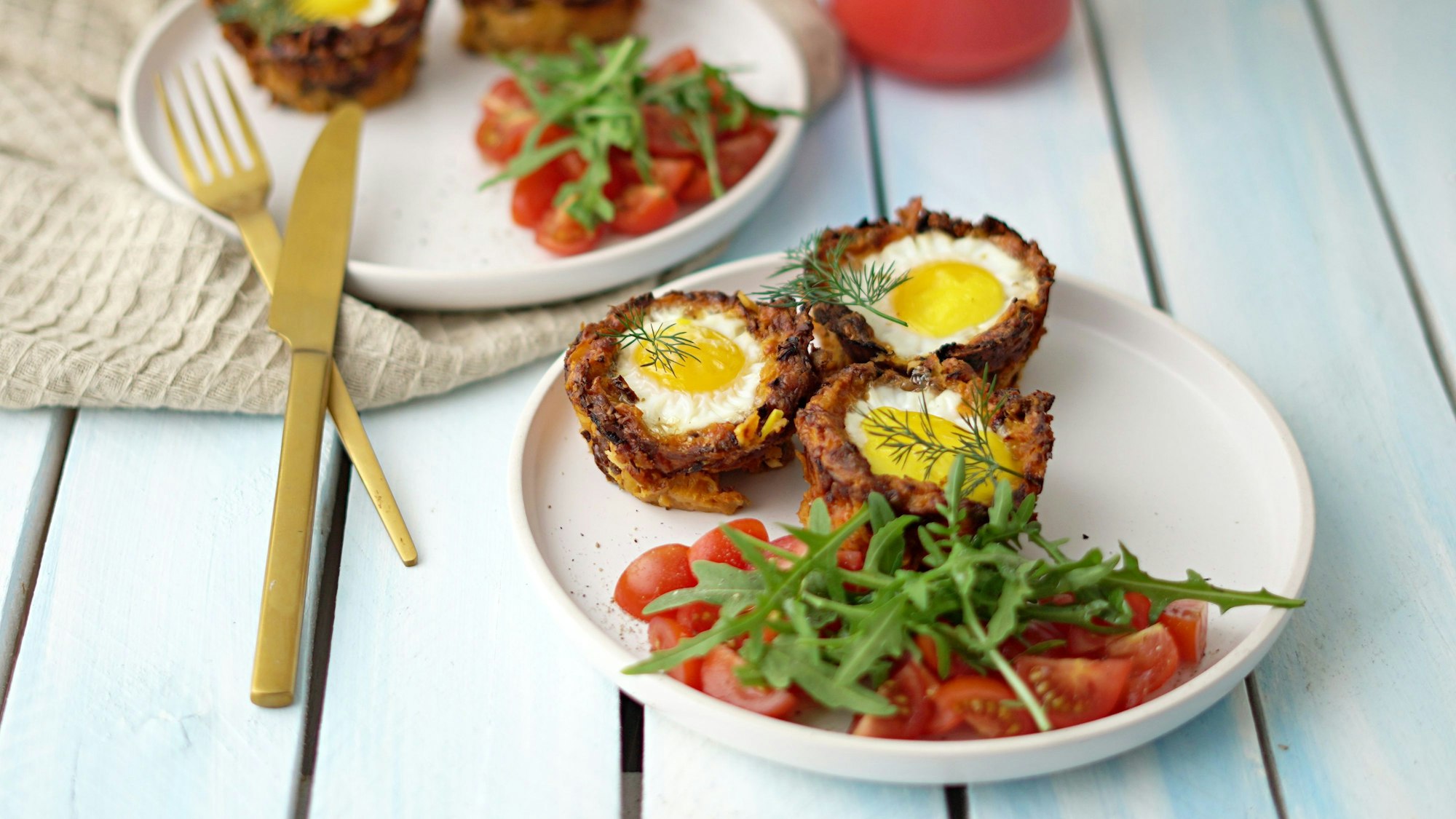 Drei Kartoffelnester stehen auf einem Teller, auf dem ebenfalls Tomatensalat angerichtet wurde.