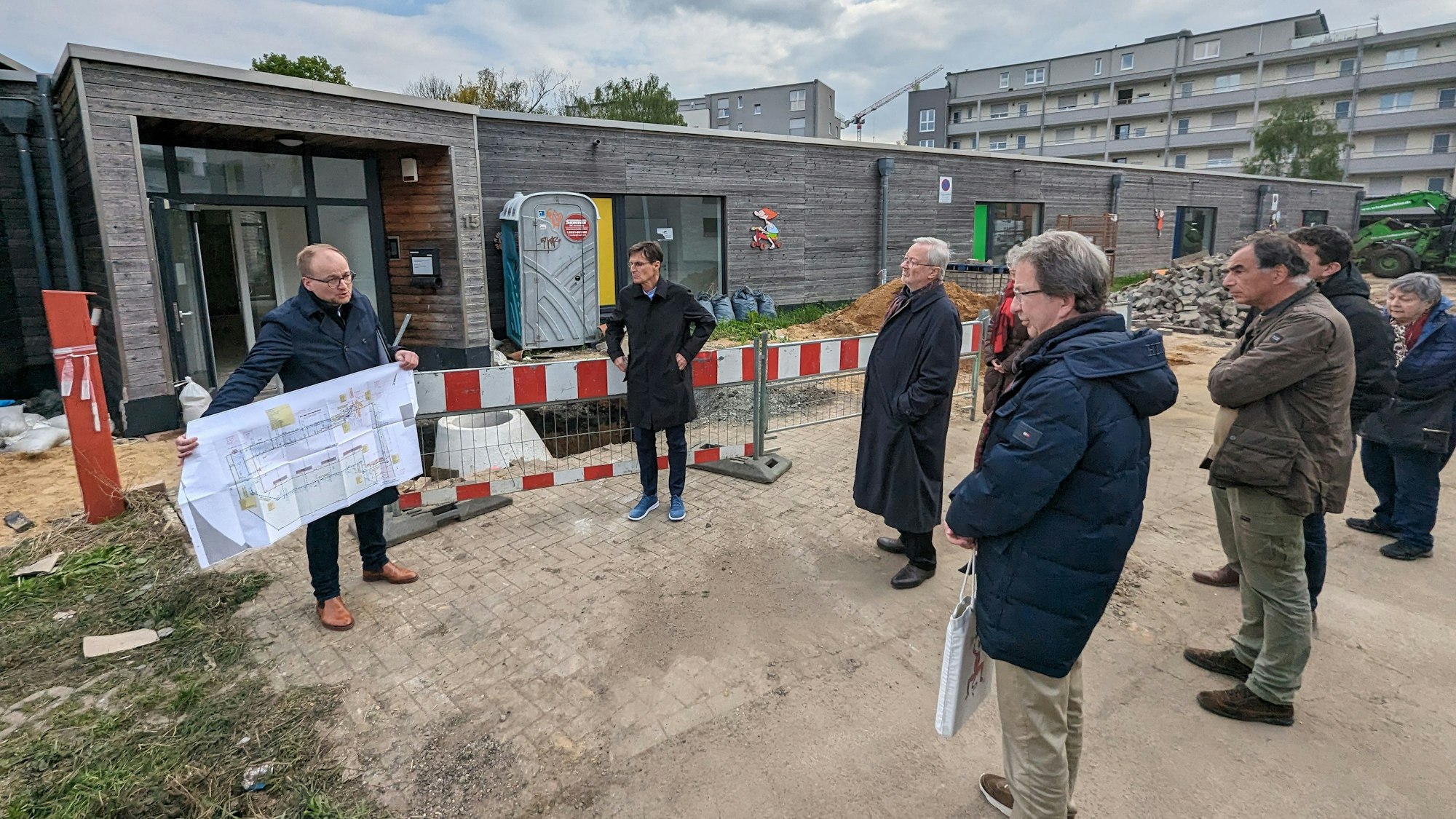 Ein Verwaltungsmitarbeiter zeigt Mitgliedern des Planungsausschusses auf der Baustelle einen Plan.