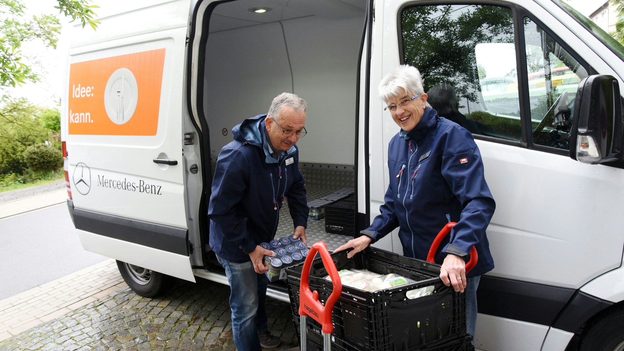 Das Foto zeigt eine Frau und einen Mann, die Lebensmittel aus einem Auto ausladen.