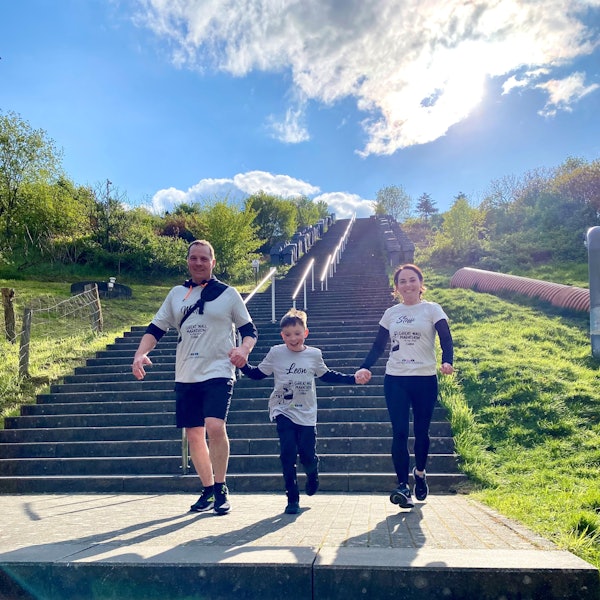 Leon Barth und seine Eltern Stefanie und Marc laufen Hand in Hand eine Treppe herunter.