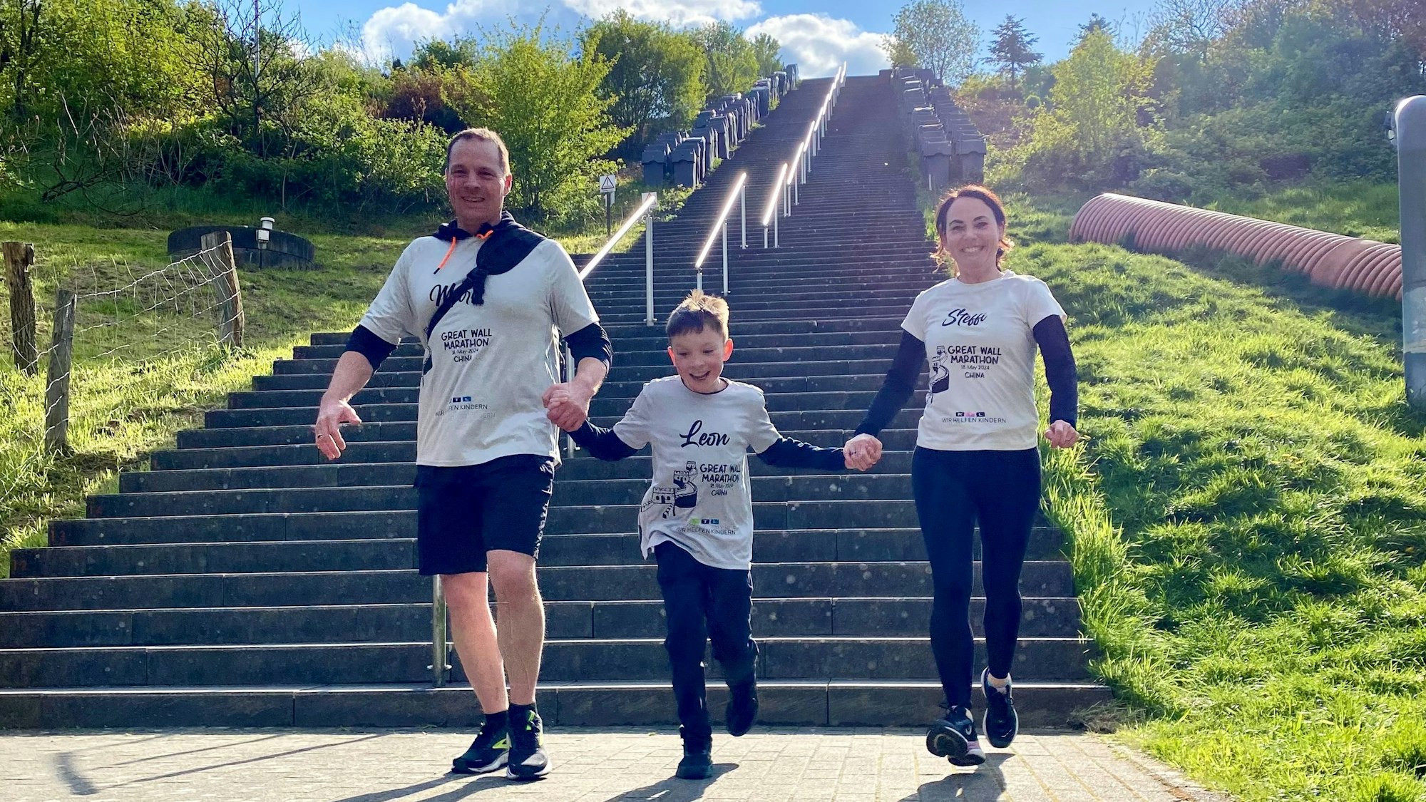 Leon Barth und seine Eltern Stefanie und Marc laufen Hand in Hand eine Treppe herunter.