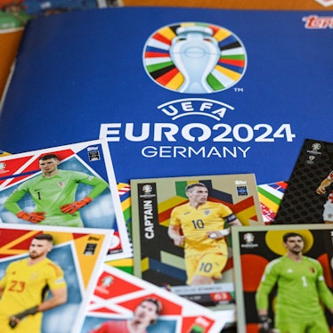 Das Sammelalbum Topps und einige Sticker zum Einkleben liegen zusammen auf einem Tisch.