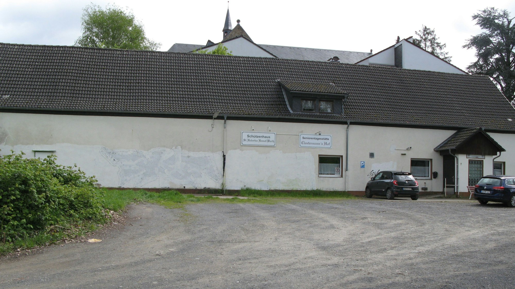 Das lang gestreckte, blassgelb gestrichene Schützenheim mit einem unbefestigten Parkplatz davor.