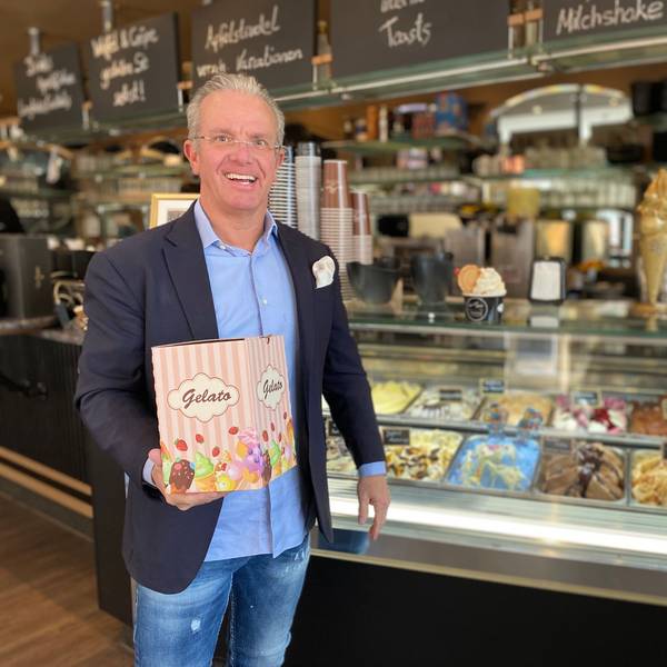 Andreas Siebrecht trägt einen Anzug. Vor der Eisauslage präsentiert er einen Pappkarton mit der Aufschrift „Gelato“.