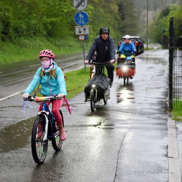 Kinder und Erwachsene auf Fahrrädern fahren entlang einer nassen Straße.