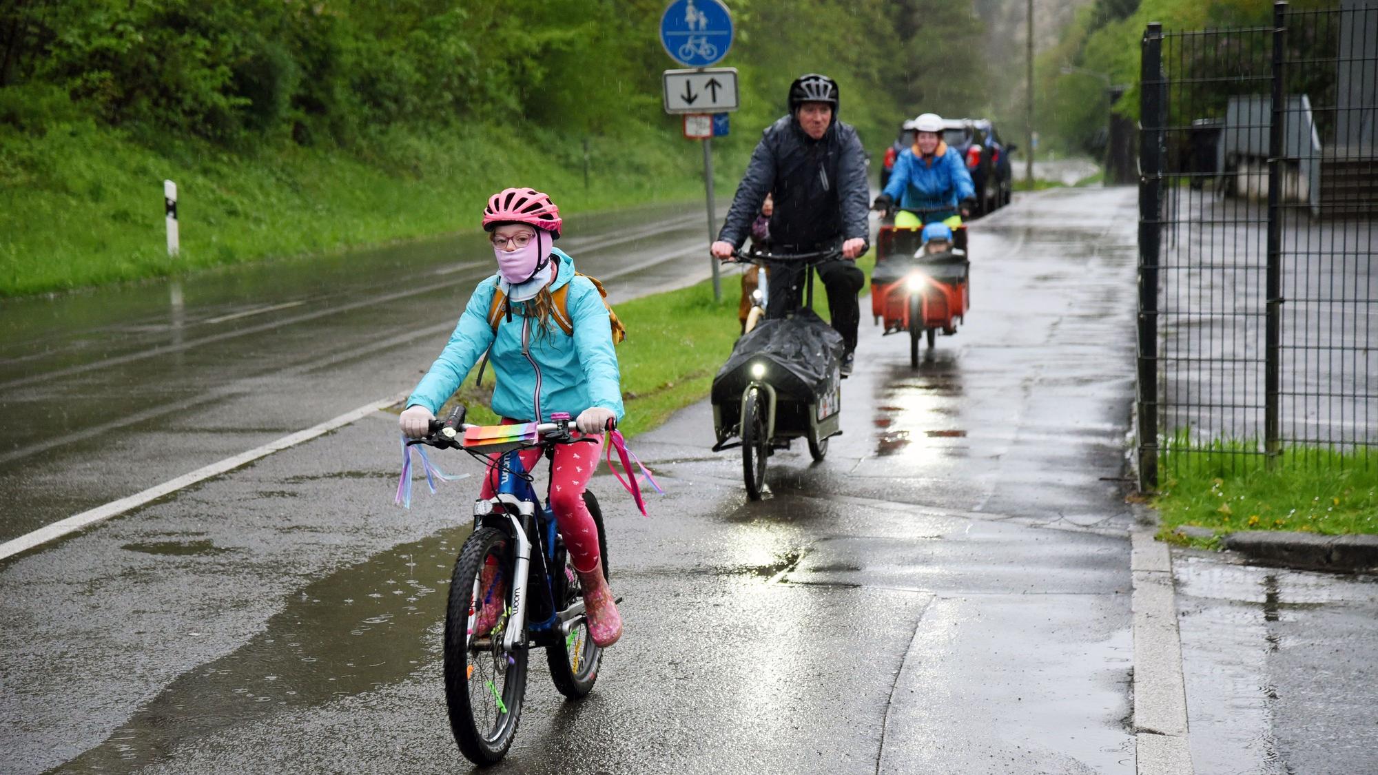 Kinder und Erwachsene auf Fahrrädern fahren entlang einer nassen Straße.