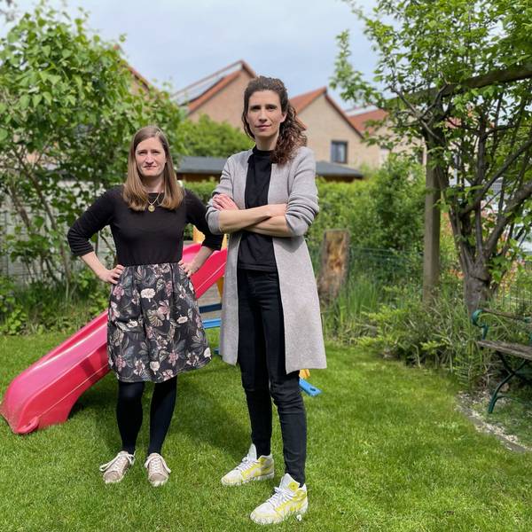 Zwei Frauen in einem Garten; im Hintergrund steht eine bunte Kinderrutsche aus Kunststoff.