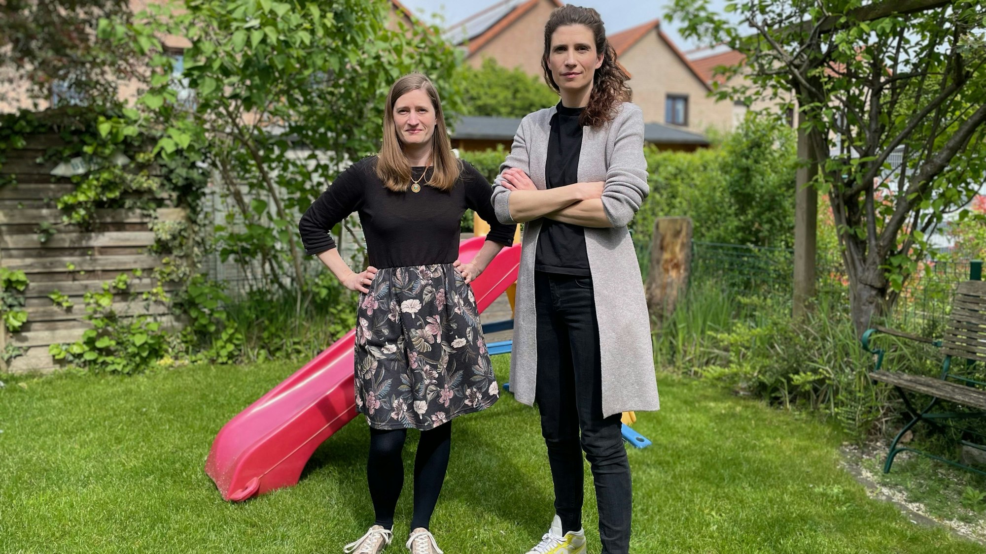 Zwei Frauen in einem Garten; im Hintergrund steht eine bunte Kinderrutsche aus Kunststoff.