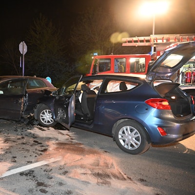 Zwei beschädigte Autos. Im Hintergrund ein Einsatzfahrzeug der Feuerwehr.