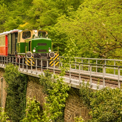 Grüne Dampflokomotive fährt über einen alten Viadukt.