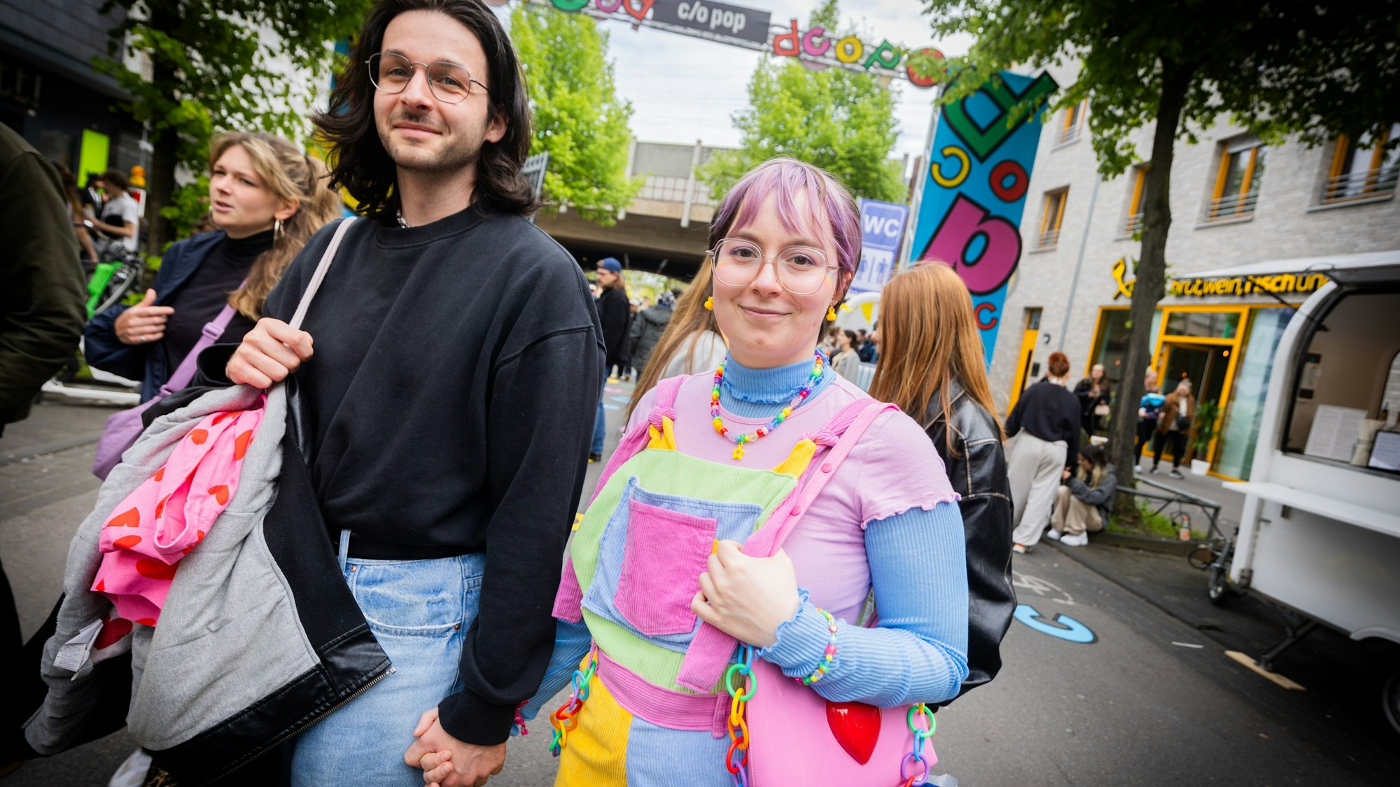 Norma und Christopher haben ihr c/o pop-Gefühl ganz individuell umgesetzt. Norma trägt kunterbunte Klamotten in Pastelltönen und eine Herzchen-Handtasche, Christopher Jeans und einen schwarzen Sweater.