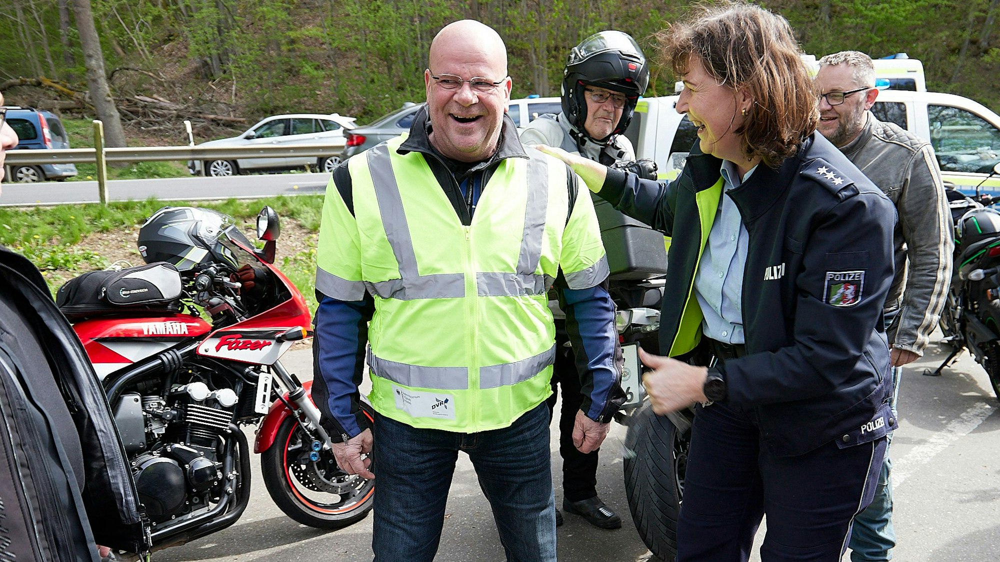 Ein Motorradfahrer trägt eine gelbe Warnweste, Polizistin Anke Weber klopft ihm auf die Schulter.
