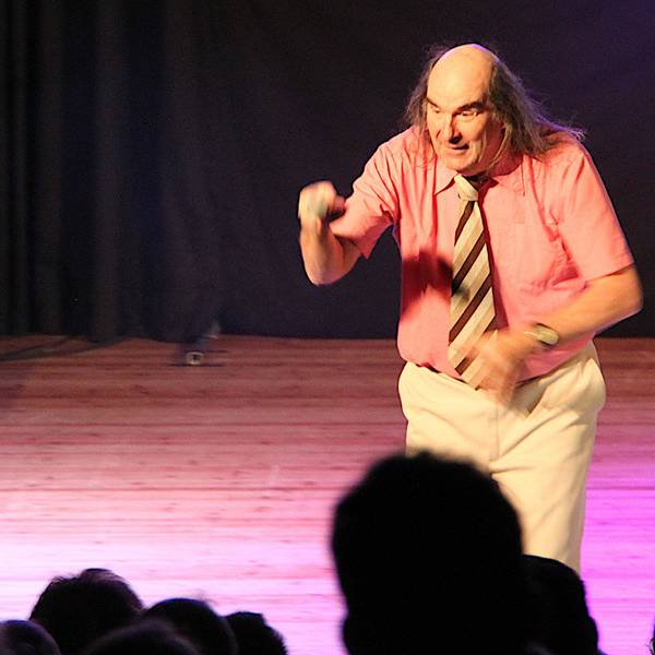 Guildo Horn steht auf der Bühne des Euskirchener Stadttheaters. Er trägt ein lachsfarbenes, kurzärmeliges Hemd mit einer braun-gestreiften Krawatte und eine helle Hose.
