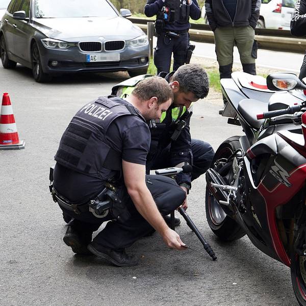 Zwei Polizisten hocken neben einem Motorrad und begutachten die Auspuffanlage.