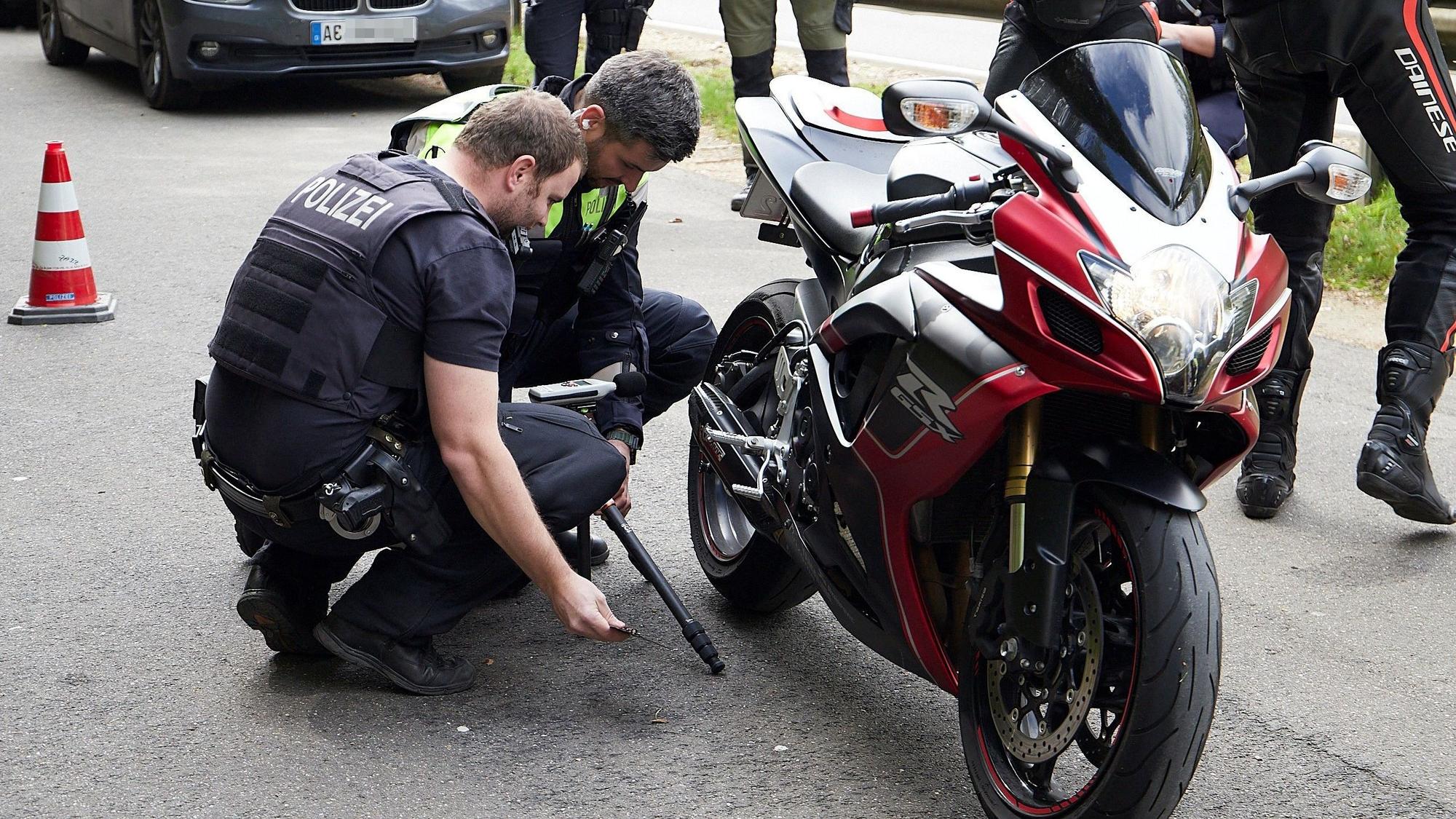 Zwei Polizisten hocken neben einem Motorrad und begutachten die Auspuffanlage.
