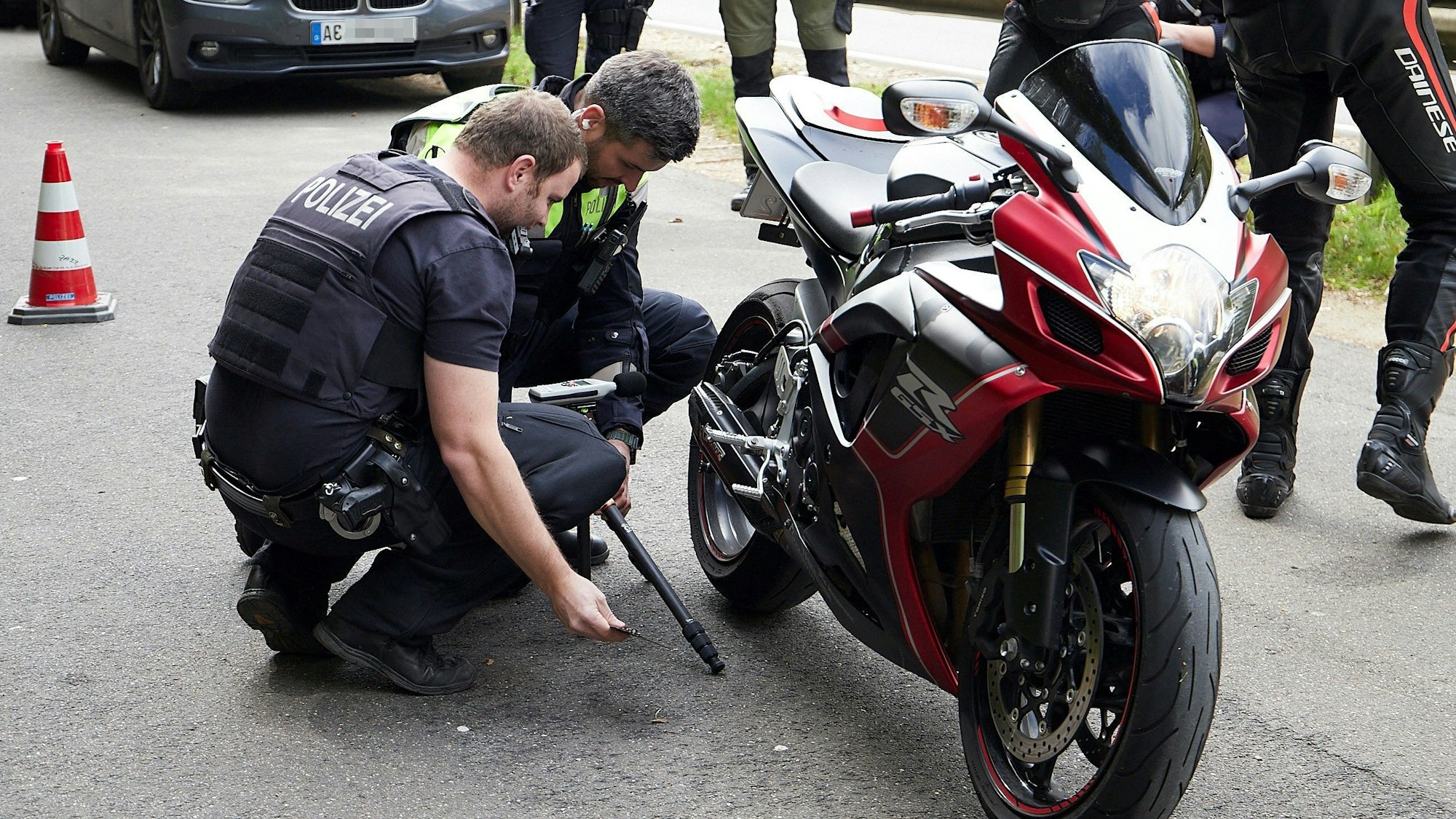 Zwei Polizisten hocken neben einem Motorrad und begutachten die Auspuffanlage.