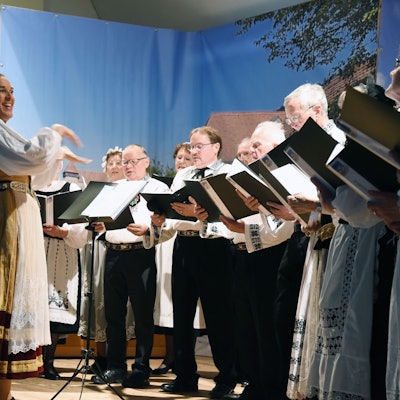 Sängerinnen und Sänger in Tracht gruppieren sich um ihre Dirigentin.