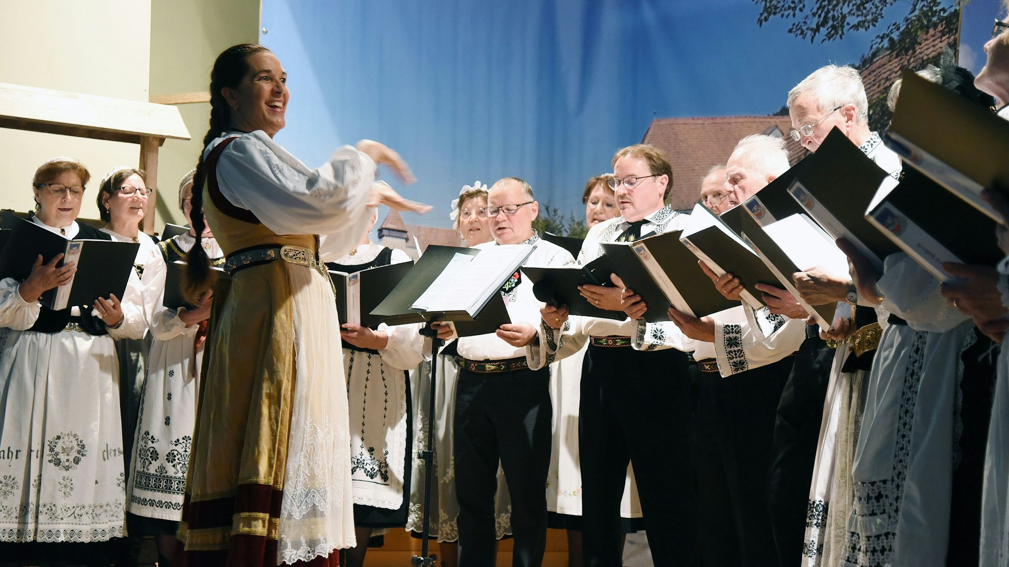 Sängerinnen und Sänger in Tracht gruppieren sich um ihre Dirigentin.