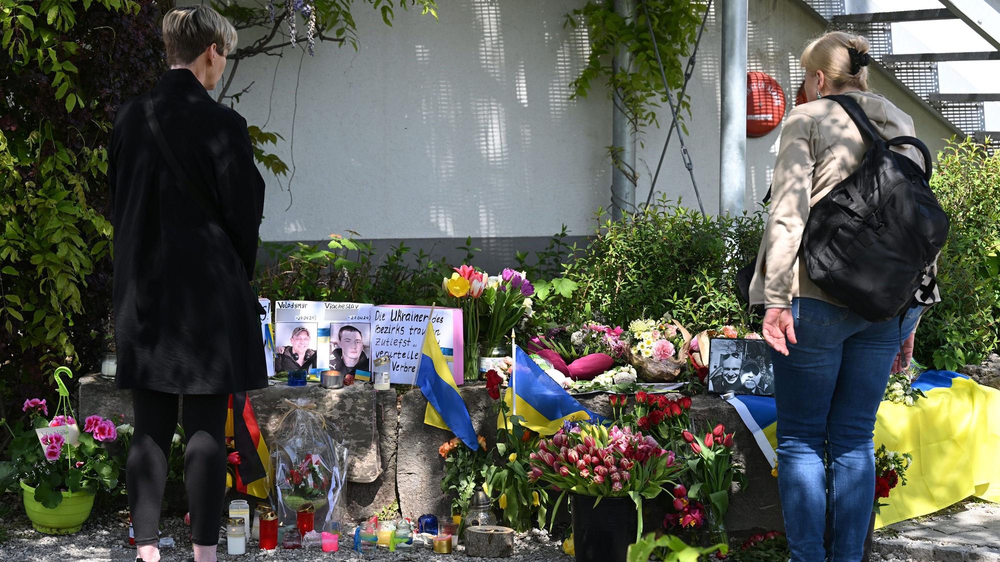Neben dem Einkaufszentrum in Murnau am Staffelsee, an dem am Samstagabend zwei Männer aus der Ukraine getötet worden sind, haben Menschen Blumen und Plakate niedergelegt.