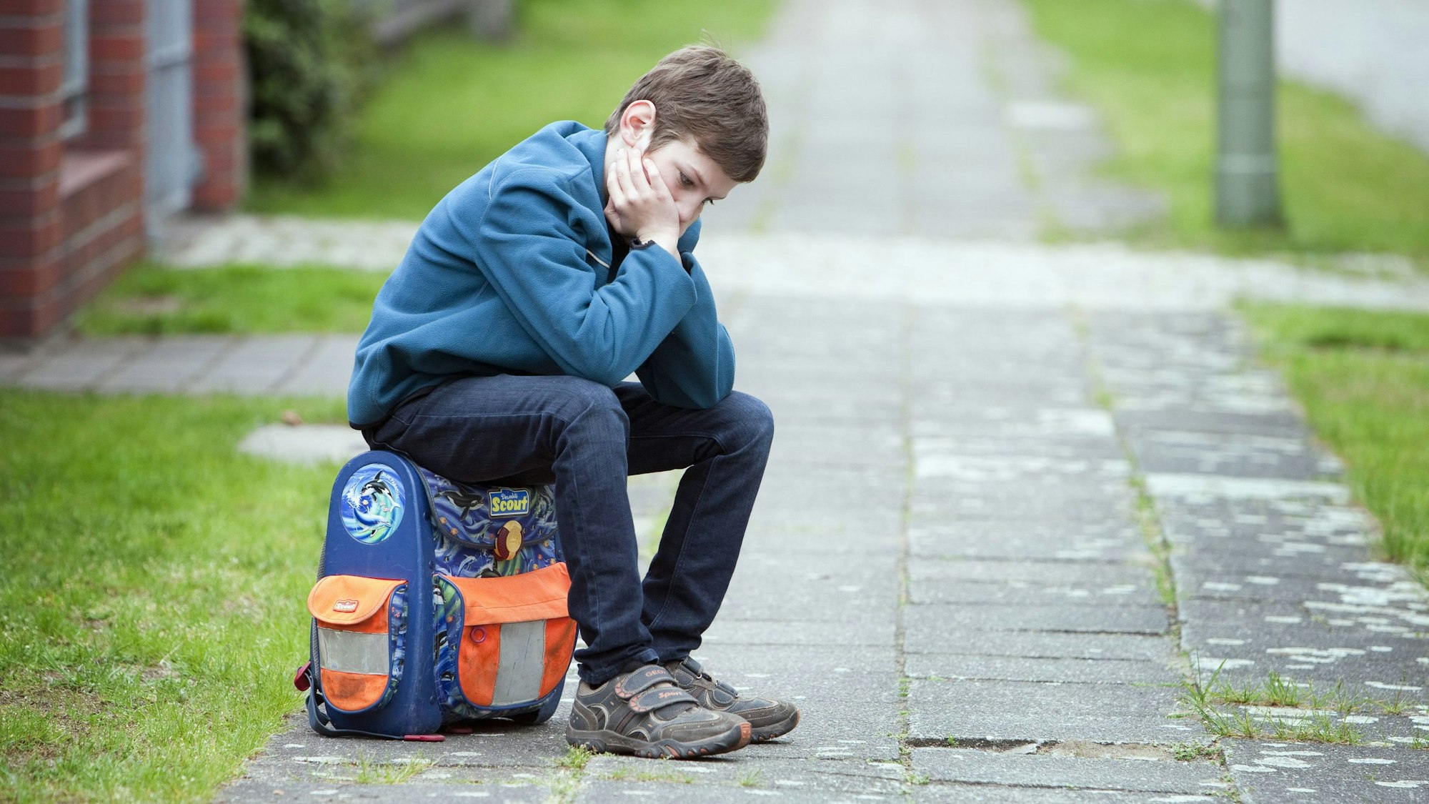 Manche Kinder schaffen es nicht, regelmäßig zur Schule zu gehen. Die Gründe dafür sind vielfältig. Ein trauriges Kind sitzt auf seinem Schulranzen.