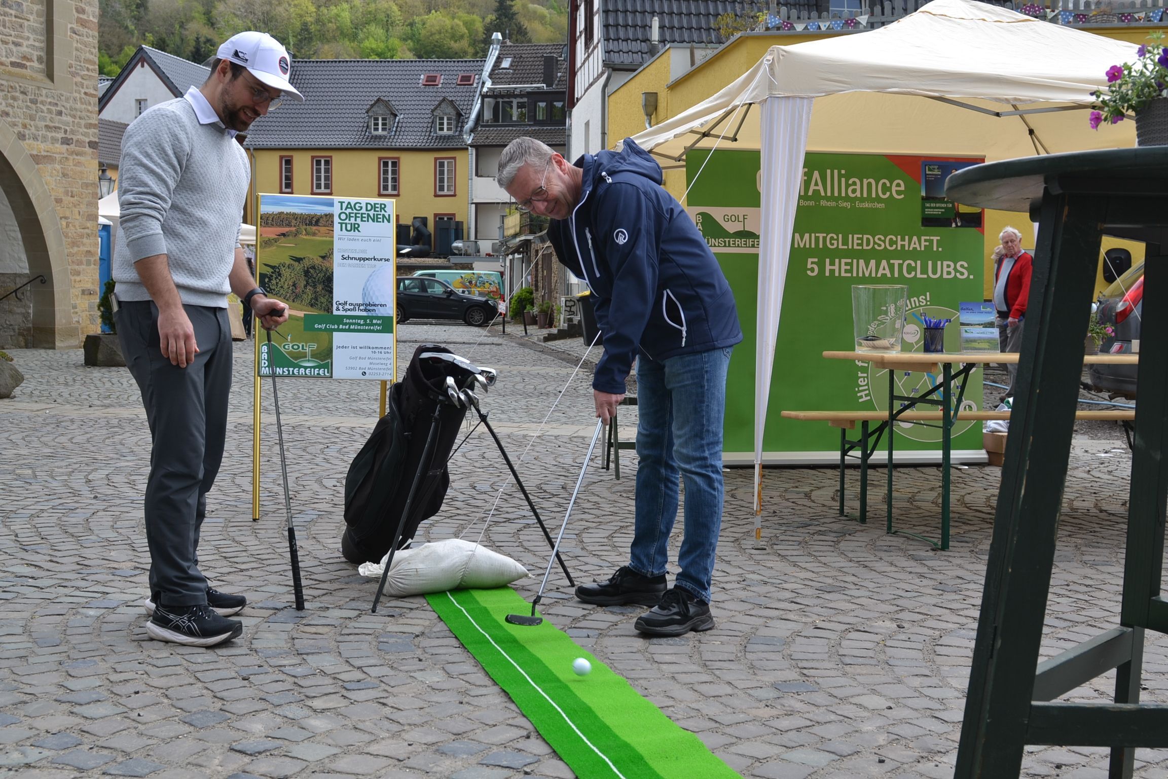 Ein Mann probiert einen Schlag auf einer kleinen Golfbahn, ein anderer schaut zu.