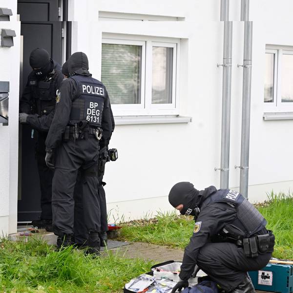 Das Bild zeigt maskierte Polizeibeamte vor einem Haus, das durchsucht wird.