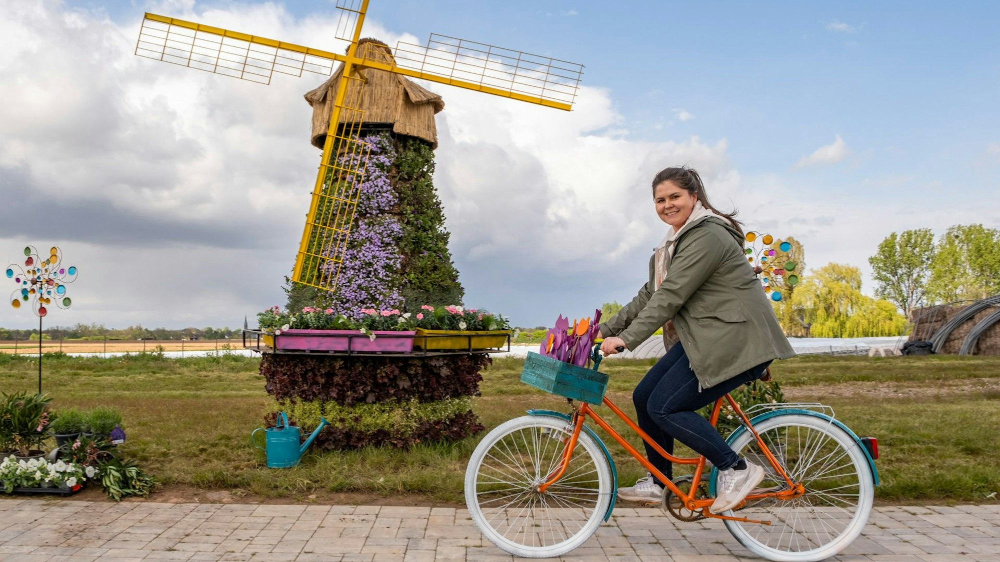 Eine Frau fährt auf dem Fahrrad vor einer Windmühle, die mit Blüten besteckt ist.