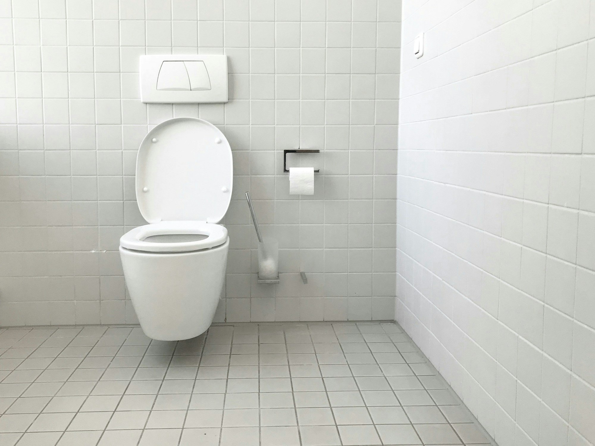 Ein weiß gekacheltes Badezimmer mit einer Toilette in der Bildmitte.